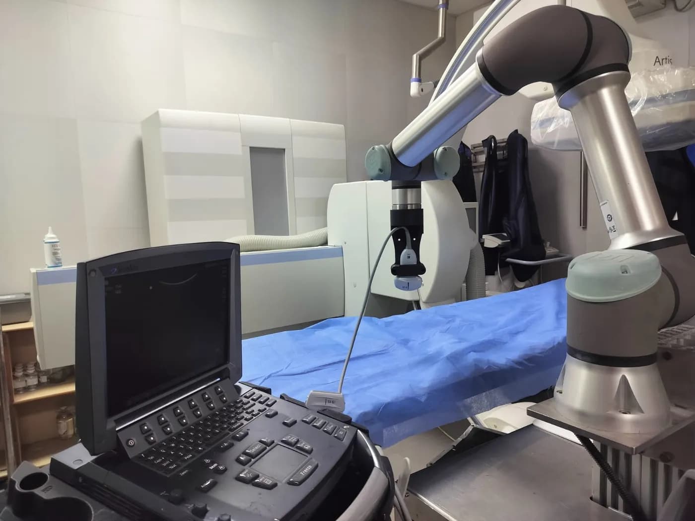 A robotic arm holding an ultrasound probe over an examination table, beside an ultrasound machine